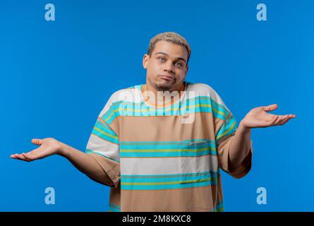 Confused man, shoulders up - can't help, makes gesture of I dont know. Difficult question, guilty reaction, puzzled guy on blue background. Stock Photo