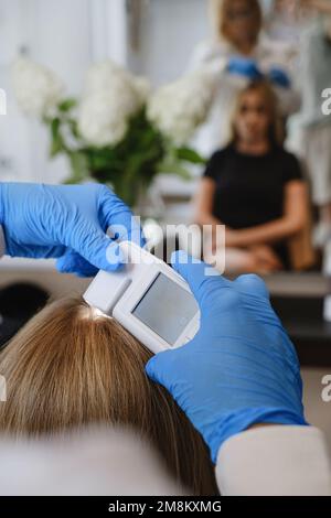 Close up view of female trihologist examines head skin of woman with special dermatology equipment system. Hairloss and trichology concept Stock Photo