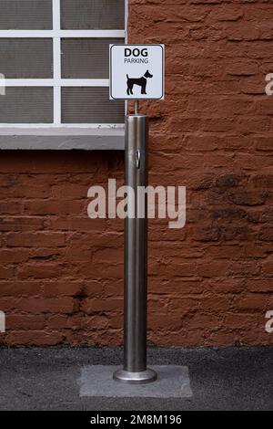 Outdoor parking area for dogs near a supermarket. White-colored sign with black dog silhouette, steel column with ring for attaching leash. Stock Photo