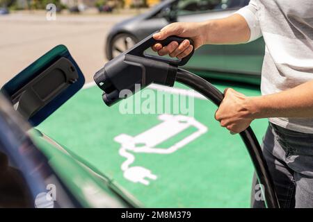 Hand inserting a DC CCS2 EV charging plug into electric car socket at charging station, Hypercharger or Supercharger.  Charge electromobility concept Stock Photo