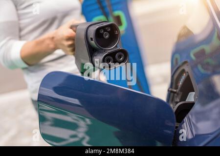 Woman inserting a DC CCS2 EV charging connector into electric car socket at charging station, Hypercharger or Supercharger.  Charge electromobility co Stock Photo