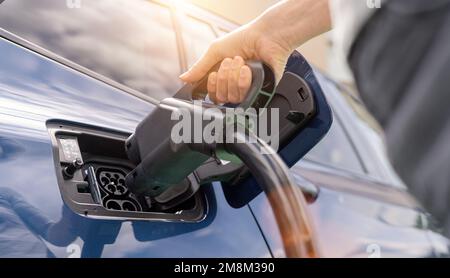 Woman inserting a DC CCS2 EV charging connector into electric car socket at charging station, Hypercharger or Supercharger.  Charge electromobility co Stock Photo
