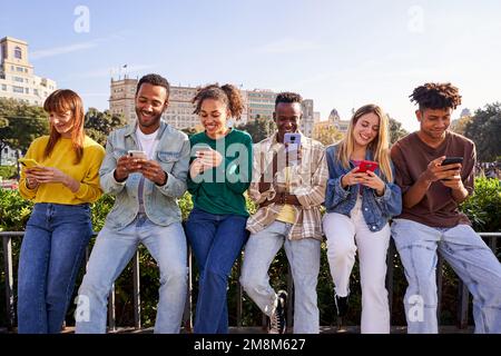 Multiethnic group of friends sitting outside using mobile phone.  Stock Photo