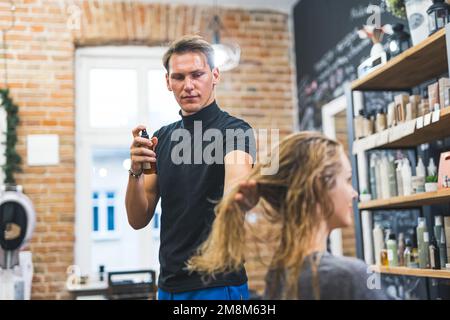 hairdresser man using spray on client's wet hair, hair care concept medium shot. High quality photo Stock Photo