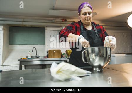 medium shot of a female baker working in the kitchen and glazing in an icing bag in front of her on the table. High quality photo Stock Photo