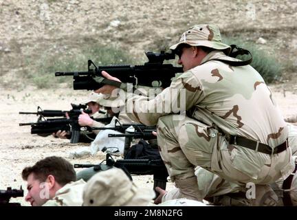 A US Navy SEAL (Squatting), from SEAL Team 8, uses the scope on his Colt 5.56mm M-4 Carbine rifle, with M203 Grenade Luncher attached, to help other SEALS sight in their weapons on a firing range in Kuwait as part of the Southwest Asia buildup. Country: Kuwait (KWT) Stock Photo