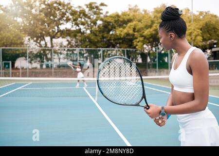 Focused young woman playing tennis with her friend. African american woman competing in a game of tennis. Professional tennis player during a match Stock Photo