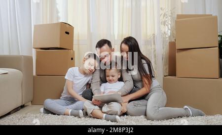 Excited family sits among boxes on floor and looks at tablet Stock Photo