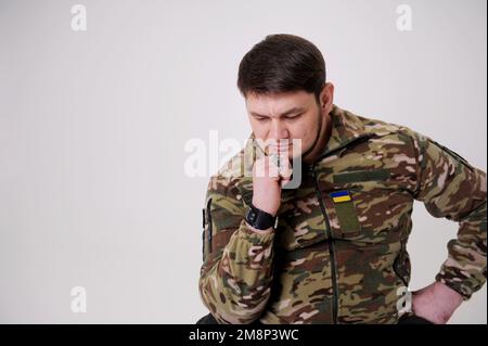 portrait of a male in camouflage coat on gray background Studio shot of young bearded ukrainian man Military serviceman at home having post traumatic stress syndrom High quality photo Stock Photo