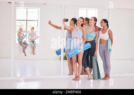 Group of friends taking a selfie in yoga studio. Young women using cellphone before yoga class. Group of happy women bonding before a workout. Young Stock Photo