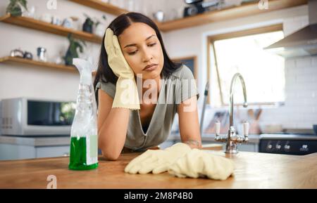 Young mixed race woman looking tired while taking a break from cleaning in the kitchen at. home. Young hispanic woman looking bored while cleaning her Stock Photo
