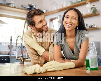 Happy young interracial couple cleaning their home. Young man and woman wearing gloves and using cleaning detergents while doing chores together at Stock Photo