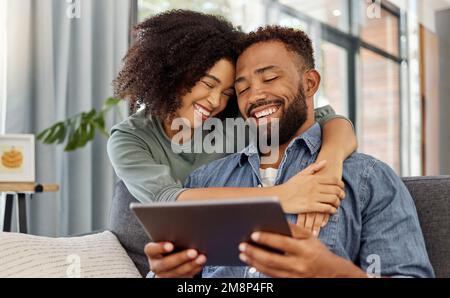 Happy young mixed race couple smiling while using a digital tablet together at home. Cheerful hispanic boyfriend and girlfriend laughing while bonding Stock Photo