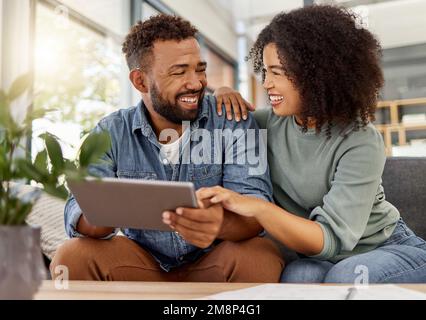 Happy young mixed race couple smiling while using a digital tablet together at home. Cheerful hispanic boyfriend and girlfriend laughing while Stock Photo