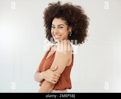 Young mixed race hispanic woman wearing and showing a bandaid on her arm standing against a white studio background. Happy young woman with a curly Stock Photo