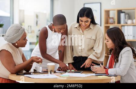 Diverse group of smiling business women using a digital tablet for a brainstorm meeting in the office. Happy confident professional team using Stock Photo