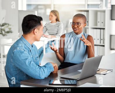 Two businesspeople having a meeting together in an office at work. Young african american businesswoman talking to an asian businessman. Colleagues Stock Photo