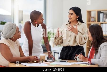 Diverse group of young ethnic business women having a meeting to brainstorm in the office. Ambitious confident professional team of colleagues talking Stock Photo
