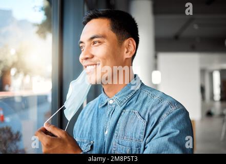Young cheerful asian businessman removing his mask while at work. One happy chinese male businessperson taking off his mask protecting from virus Stock Photo