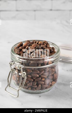 Pine nuts in a jar and a pine cone in the kitchen on a light background. The concept of organic food and protein food Stock Photo