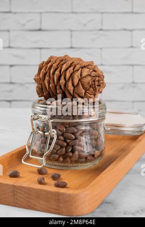 Pine nuts in a jar and a pine cone in the kitchen on a light background. The concept of organic food and protein food Stock Photo