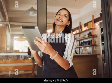 Businesswoman ordering stock on her digital tablet. Business owner using an online digital app in her cafe. Happy boss using a wireless device in her Stock Photo