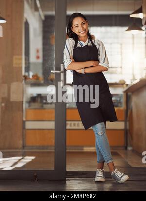 Portrait of confident businesswoman leaning on her business door. Young boss arms crossed in her store entrance. Business assistant standing in her Stock Photo