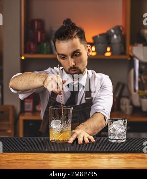 Young barman stirring fresh alcoholic cocktail with sweet fruit syrup on the bar counter Stock Photo