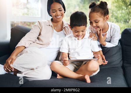 Happy young hispanic family sitting together and using tablet. Curious cute little girl and boy sitting with their mother and learning watching videos Stock Photo