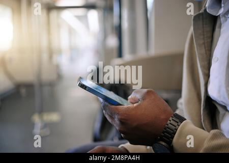 Closeup of Black businessman travelling in a train while using a cellphone. African american male using a wireless device while commuting on a train Stock Photo