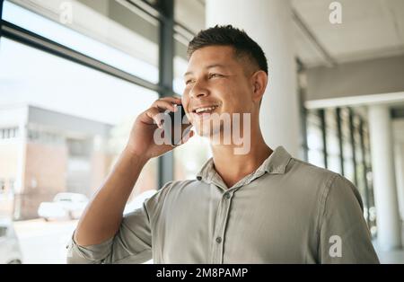 Close up of business man looking out window while talking on the phone. Young entrepreneur making or answering call in office Stock Photo