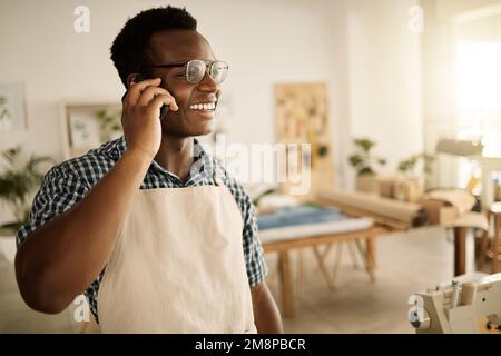 Smiling designer making a phone call in his studio. Fashion designer talking during a cellphone call. Small business owner using his smartphone Stock Photo