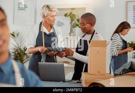 Two clothing designers using a laptop while working with material in a meeting at work. Young female african american tailor talking while working Stock Photo