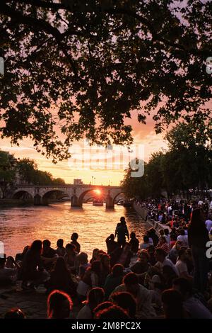 Paris, France - May, 2022: Crowd People have picnic on seine river bank at sunset in Le Marais Stock Photo