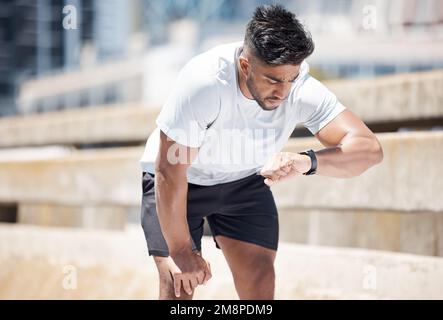 Athletic young mixed race man looking at his watch while exercising outdoors. Handsome mixed race male looking serious while checking the time on his Stock Photo