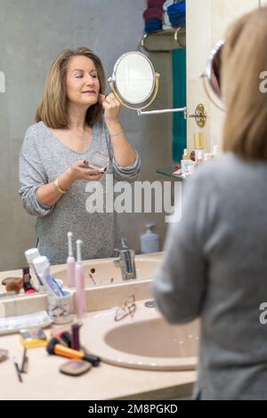 Mature white woman applying beauty treatments in front of the mirror of her bathroom Stock Photo