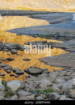 The golden cliffs, in the early morning light, reflecting in Calm rocky pools in the Fish River Canyon, Namibia Stock Photo