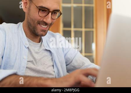 Young male with glasses smiling while using laptop Stock Photo