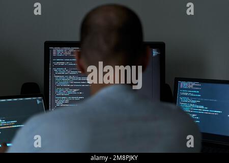 Young male writing coding on three screens. Software programmer and web developer Stock Photo