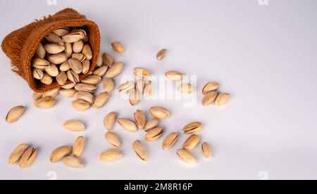 Sack With Pistachios On Isolated On A White Background. Pistachios Pouring From A Small Sack On A White Table. Stock Photo