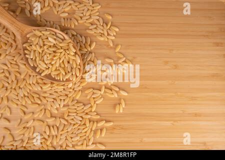 Grains Of Barley Noodle On A Wooden Floor, Top View. Raw Barley Noodle in Wooden Spoon For Menu Concept, Copy Space. Stock Photo