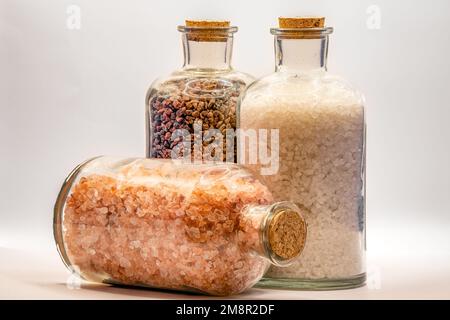 three glass jars with cork lids containing white, pink and brown natural salt rock granules Stock Photo