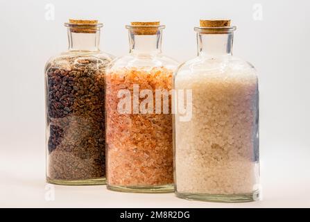 three glass jars with cork lids containing white, pink and brown natural salt rock granules Stock Photo
