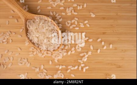 Grains Of Rice On A Wooden Floor, Top View. Raw Rice in Wooden Spoon For Menu Concept, Copy Space. Stock Photo