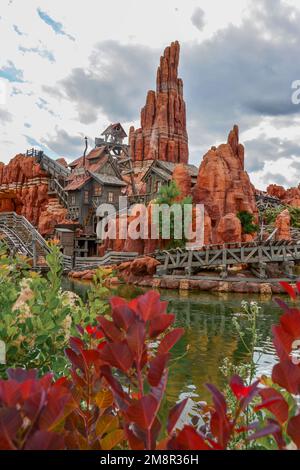 A vertical shot of the Big Thunder Mountain Railroad Rollercoaster with colorful plants near it in Disneyland of Paris Stock Photo