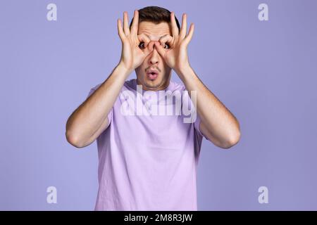Young handsome man doing gesture like binoculars Stock Photo