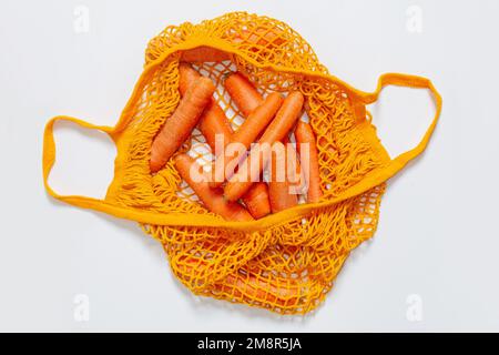 Mesh reusable bag with fresh carrots. Orange string bag. Raw carrots. View from above. Vegetarian, raw food, fresh vegetables. Conscious consumption. Stock Photo