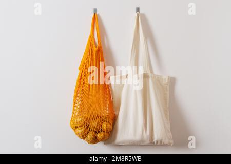 mesh grocery bag. Reusable bag. Vegetarianism, raw food diet, conscious consumption, grid. orange mesh bag hanging on a hook. Several shopping bags. W Stock Photo