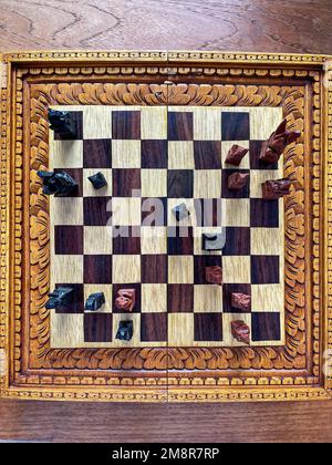 Top view of a chessboard with handmade carved pieces. Black and white shapes. Intelligent game. Competitive spirit. Stock Photo