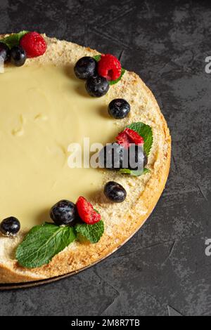 Homemade classic cheesecake on a dark background. Decorating a sweet cake with fresh berries, mint leaves Stock Photo